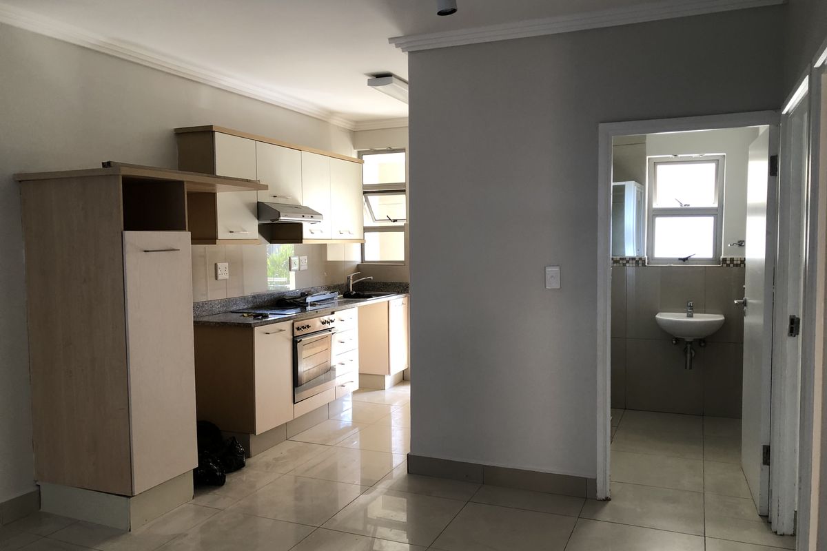 An open-plan kitchen area featuring built-in cabinetry, granite countertops, and an integrated oven, with an adjacent bathroom visible through the doorway.