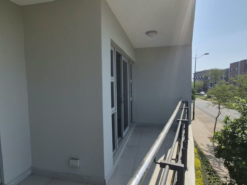 A clean, modern balcony featuring tiled flooring, a metal balustrade, and sliding glass door access, offering an elevated view of the surrounding neighborhood.