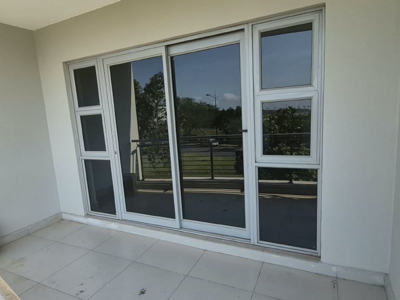 A clean, covered balcony featuring tiled flooring, a metal balustrade, and large sliding glass doors providing access to the interior.