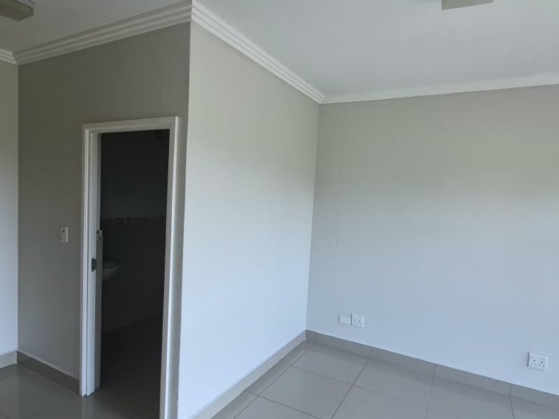 A clean, empty bedroom featuring neutral wall paint, tiled flooring, built-in cupboards, and direct access to an adjoining bathroom.