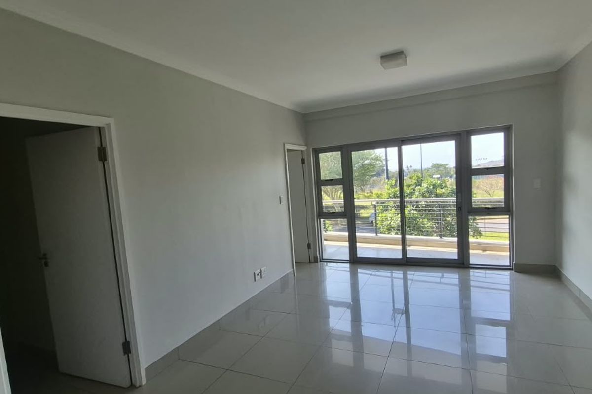 A bright, empty living room featuring neutral tiled flooring and large sliding glass doors that open onto a balcony.
