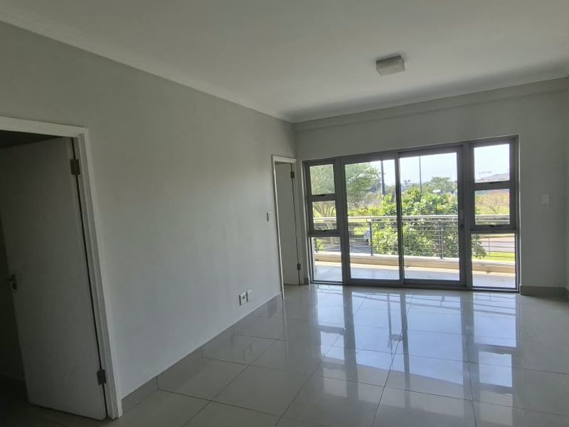 A bright, empty living room featuring neutral tiled flooring and large sliding glass doors that open onto a balcony.