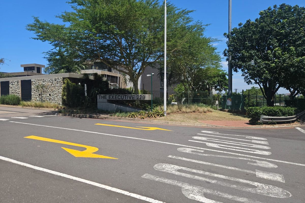 Street view of the entrance to The Executive 220 residential complex, featuring stone wall detailing and established landscaping.