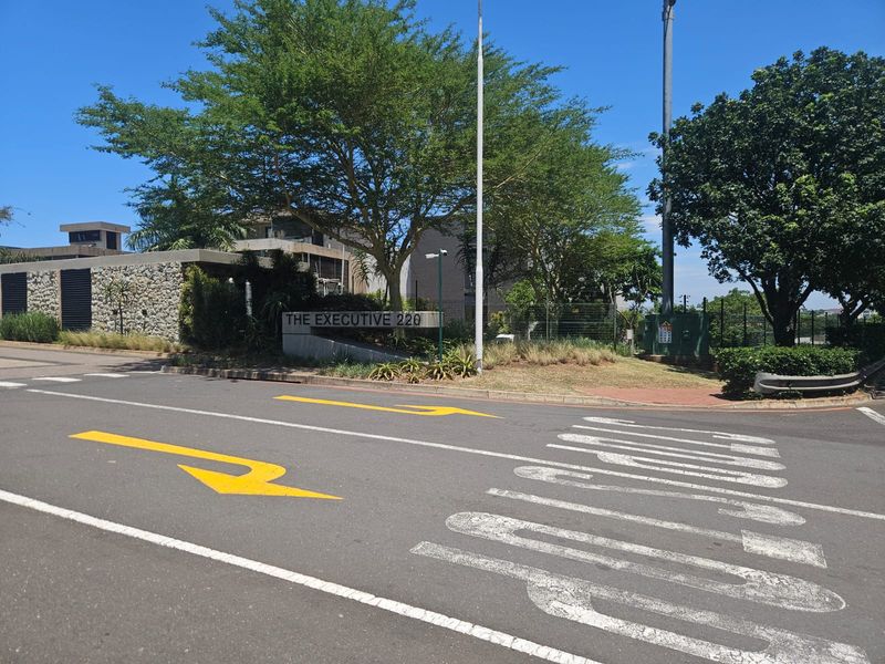 Street view of the entrance to The Executive 220 residential complex, featuring stone wall detailing and established landscaping.