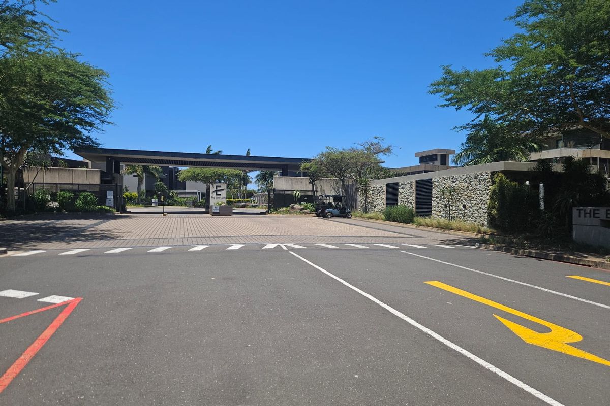 View of the secure entrance gatehouse and paved driveway leading into the residential estate.