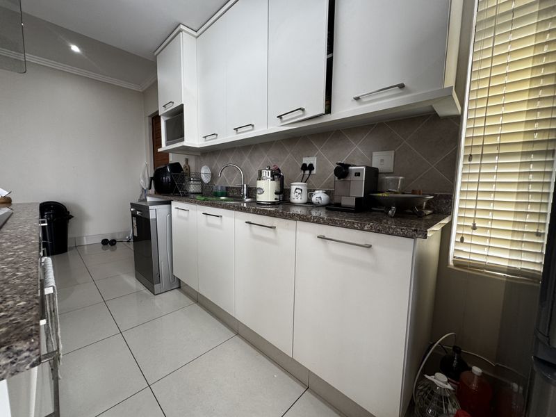 A functional kitchen featuring white cabinetry, granite countertops, a tiled backsplash, and neutral floor tiles, providing a clean and practical workspace.