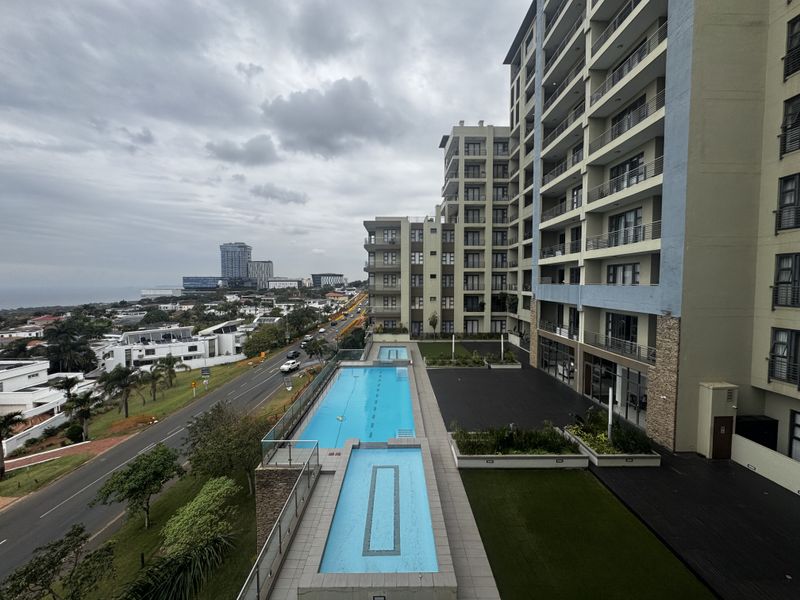 Elevated view of the apartment complex featuring a swimming pool, wading pool, landscaped garden areas, and modern building facade with balconies.