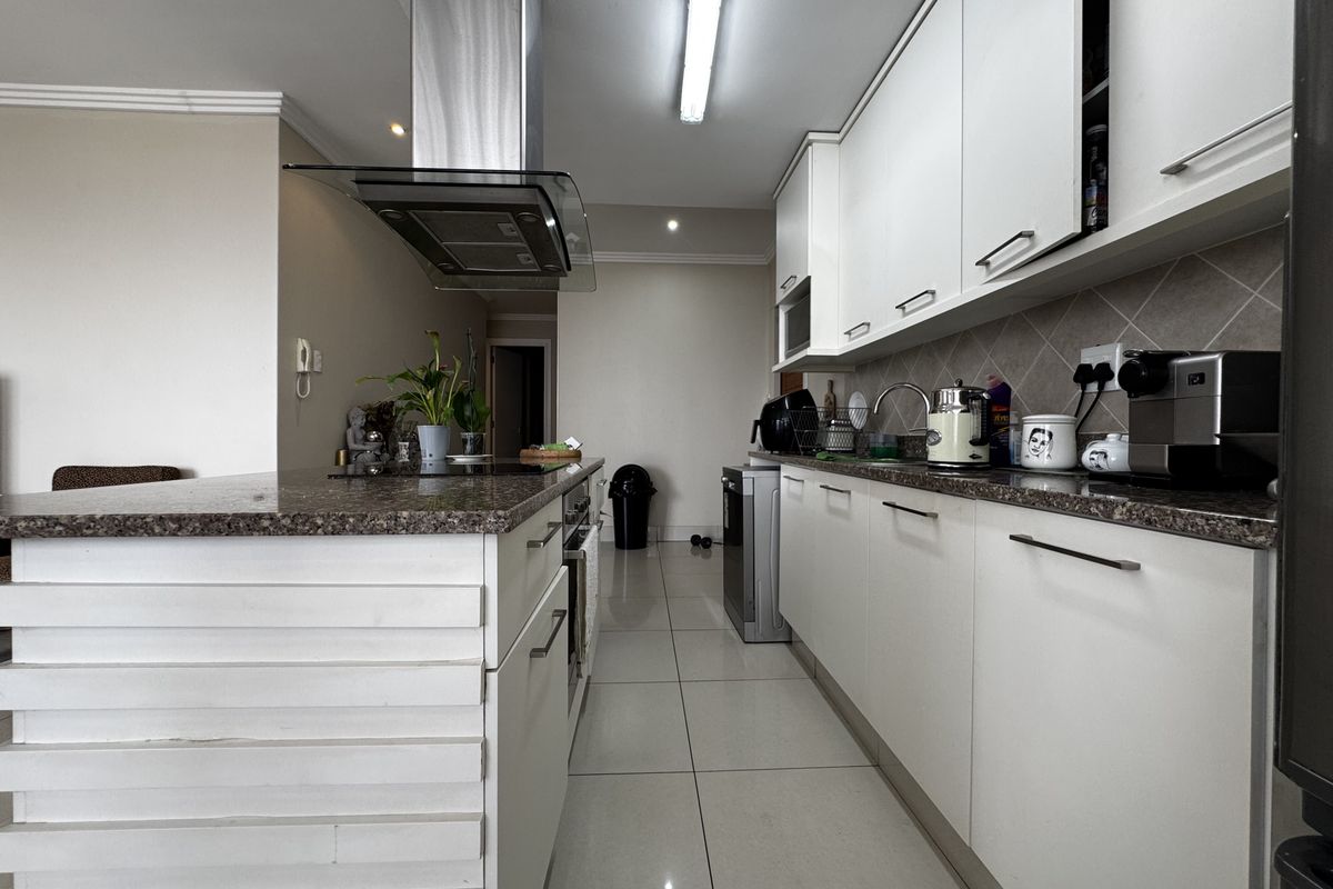 Modern kitchen featuring white cabinetry, granite countertops, stainless steel extractor fan, and tiled flooring, offering a clean and functional workspace.