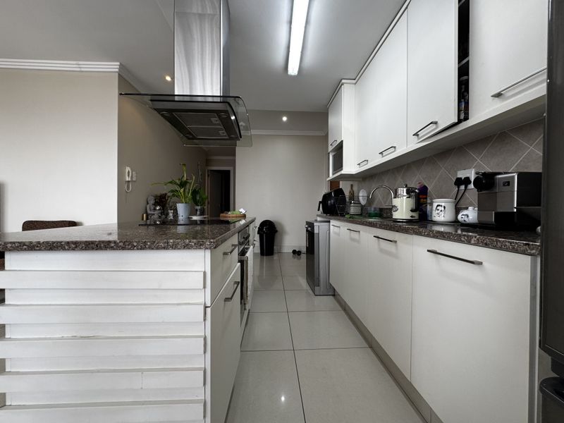 Modern kitchen featuring white cabinetry, granite countertops, stainless steel extractor fan, and tiled flooring, offering a clean and functional workspace.