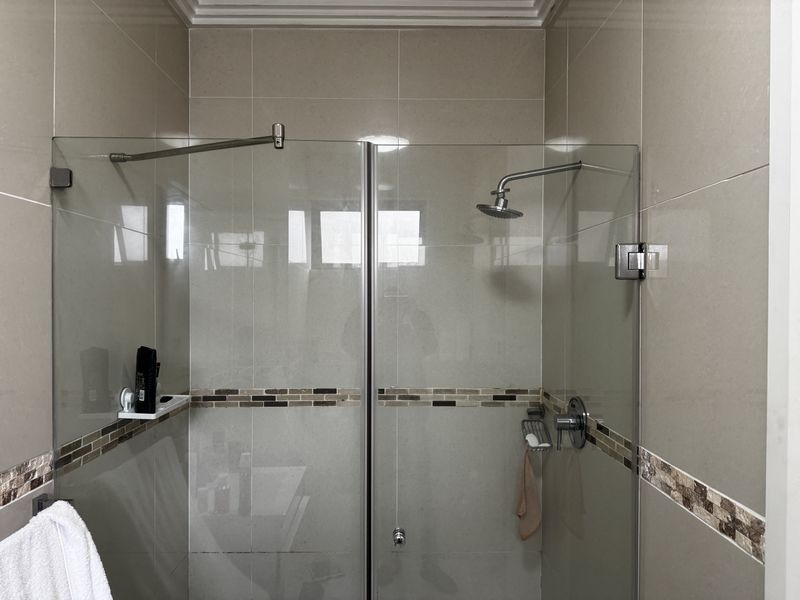 A modern bathroom shower featuring a glass enclosure, wall-mounted shower head, and neutral-toned tiling with a decorative mosaic accent border.