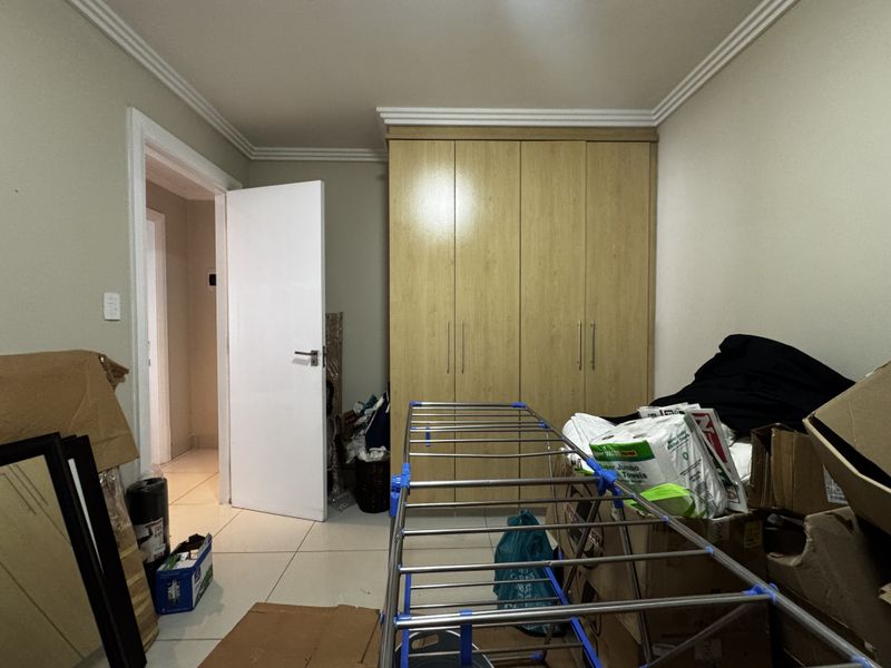 A bedroom featuring built-in wooden cupboards, tiled flooring, and decorative ceiling cornicing.