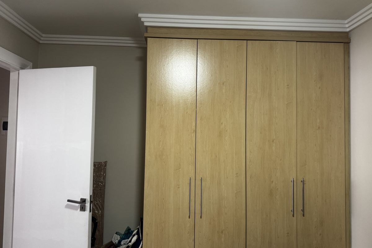 A bedroom featuring a large, light wood-finish built-in wardrobe with modern handles and decorative crown molding.