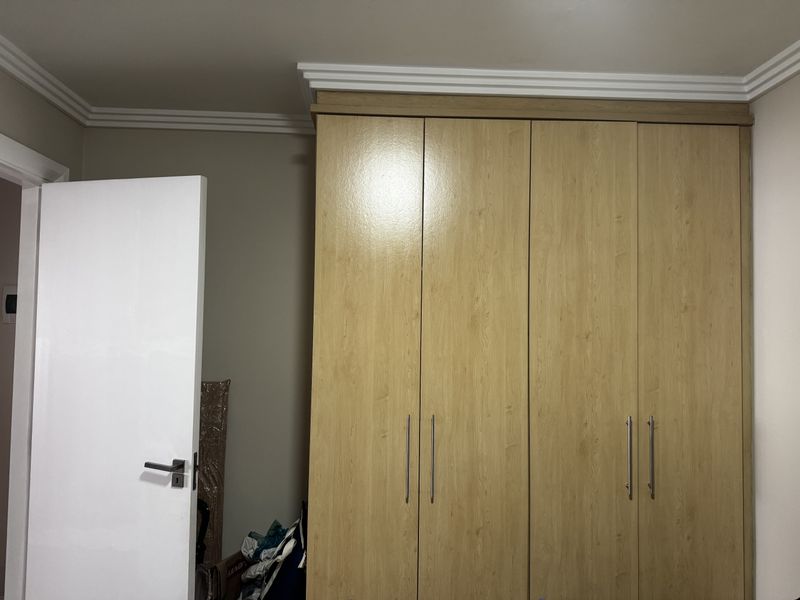 A bedroom featuring a large, light wood-finish built-in wardrobe with modern handles and decorative crown molding.