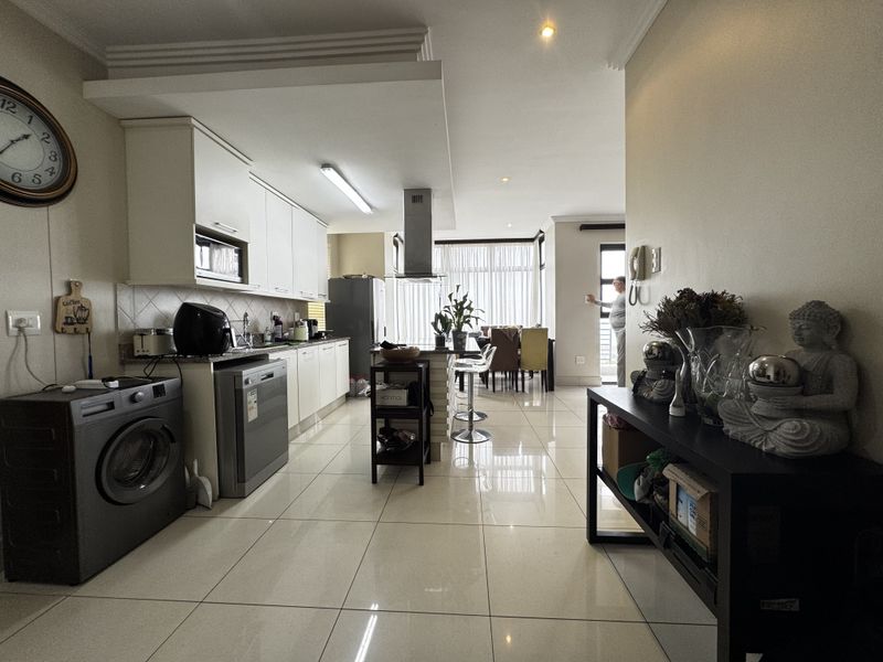 Open-plan kitchen and living area featuring modern white cabinetry, stone countertops, tiled flooring, and integrated lighting, creating a bright and functional living space.