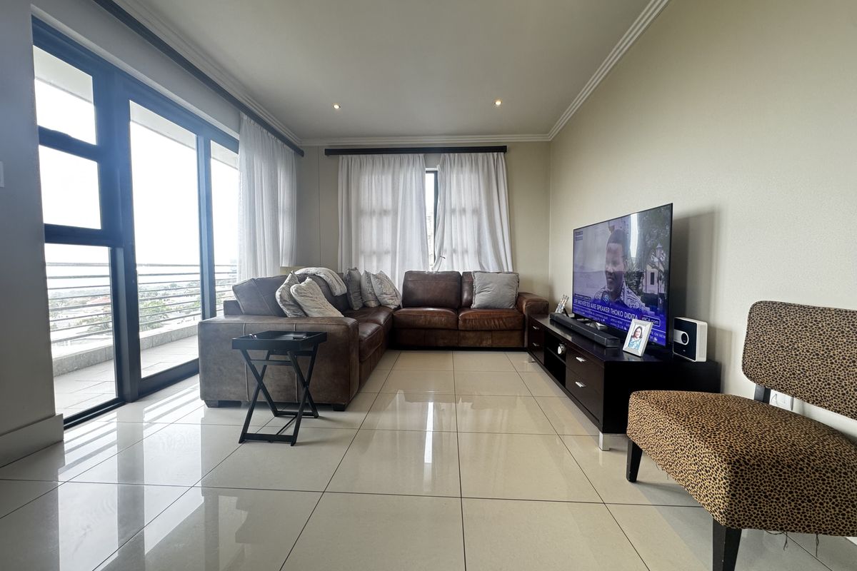 Spacious living room featuring large format floor tiles, recessed downlighting, and expansive sliding glass doors providing access to the balcony.