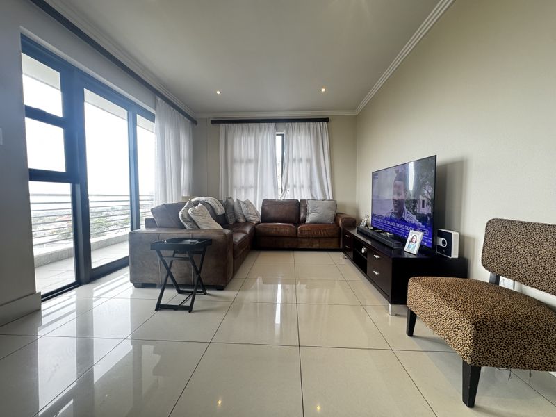 Spacious living room featuring large format floor tiles, recessed downlighting, and expansive sliding glass doors providing access to the balcony.