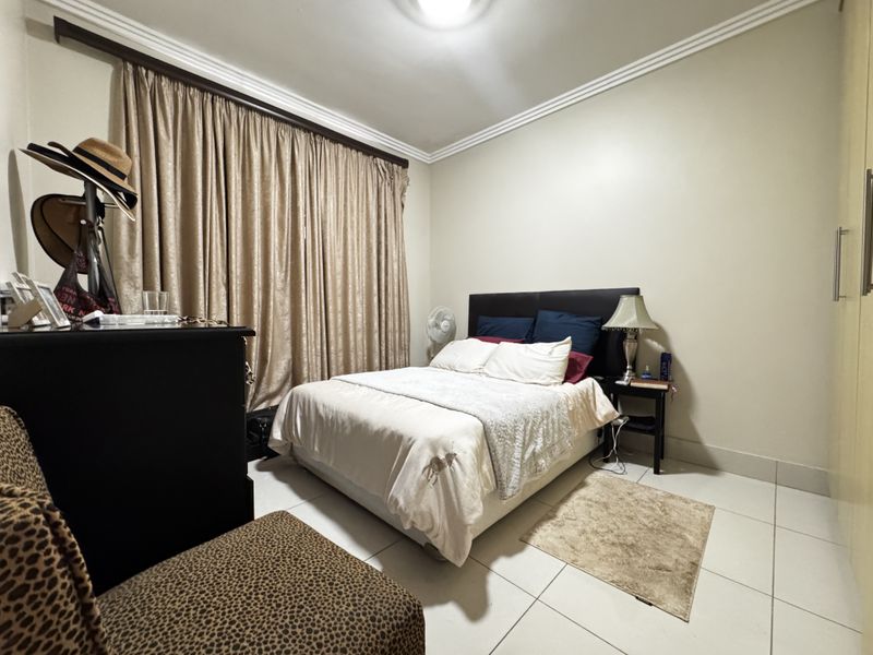 A well-proportioned bedroom featuring tiled flooring, built-in cupboards, and decorative ceiling cornicing, offering a functional and comfortable living space.