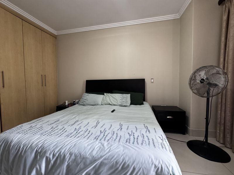 A functional bedroom featuring built-in wooden wardrobes, neutral wall finishes, and tiled flooring, providing a clean and practical living space.