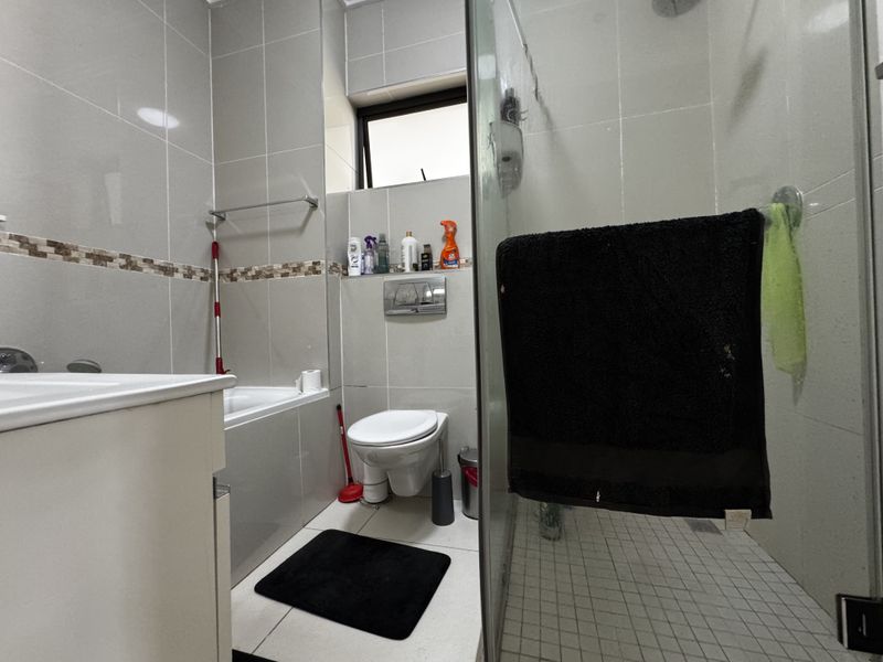 Modern bathroom featuring a wall-mounted toilet, a built-in bathtub, and a separate glass-enclosed shower with neutral floor-to-ceiling tiling.