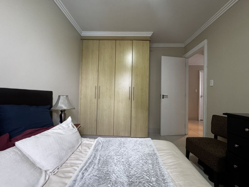 A well-maintained bedroom featuring neutral walls, crown molding, tiled flooring, and a large built-in wooden wardrobe.