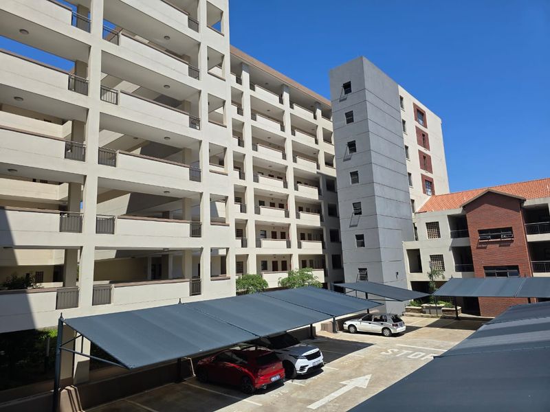 Exterior view of a multi-story apartment complex featuring covered parking bays and a paved driveway area.