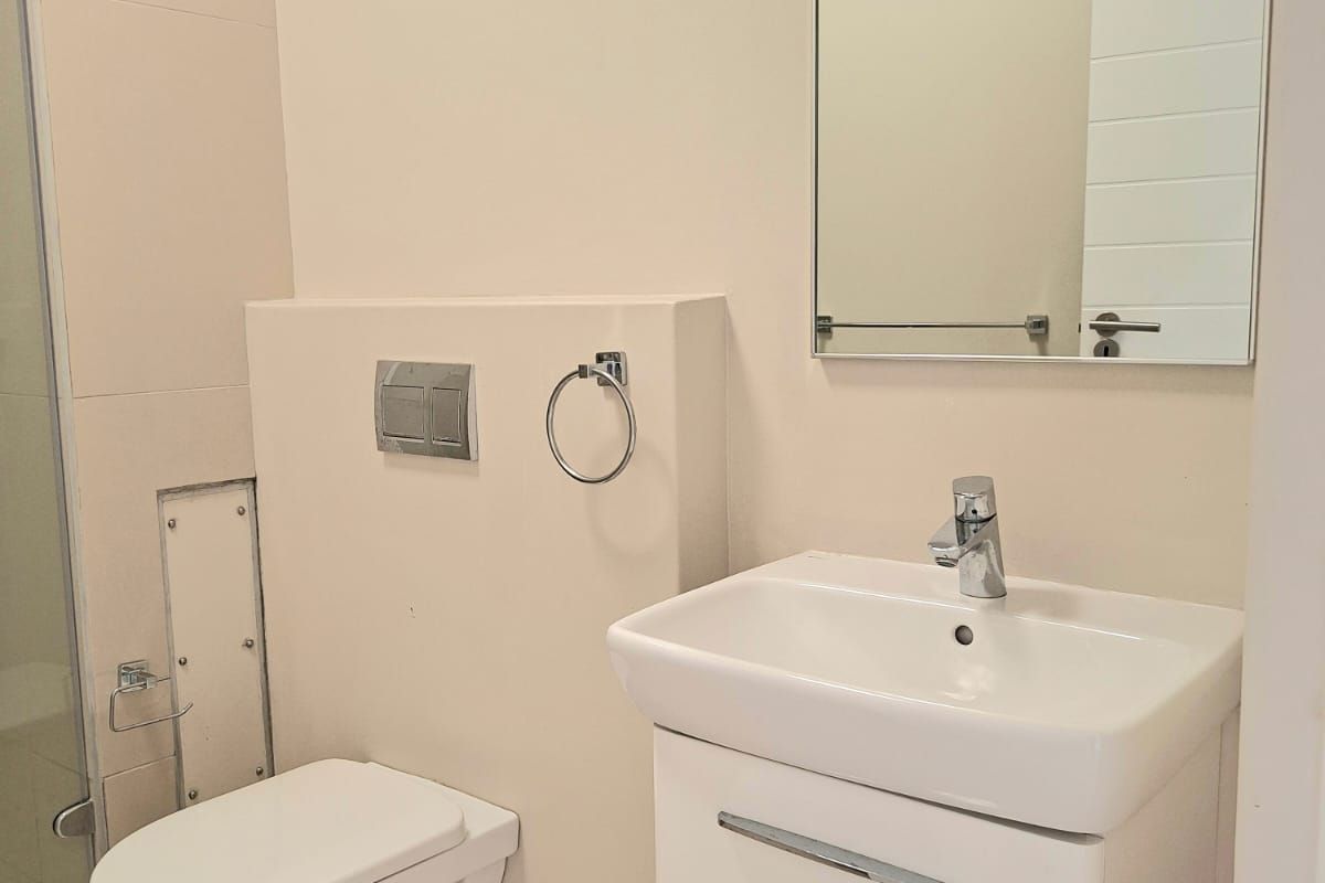 Modern bathroom featuring a wall-hung toilet, vanity basin with mixer tap, wall mirror, and a glass shower enclosure with tiled finishes.