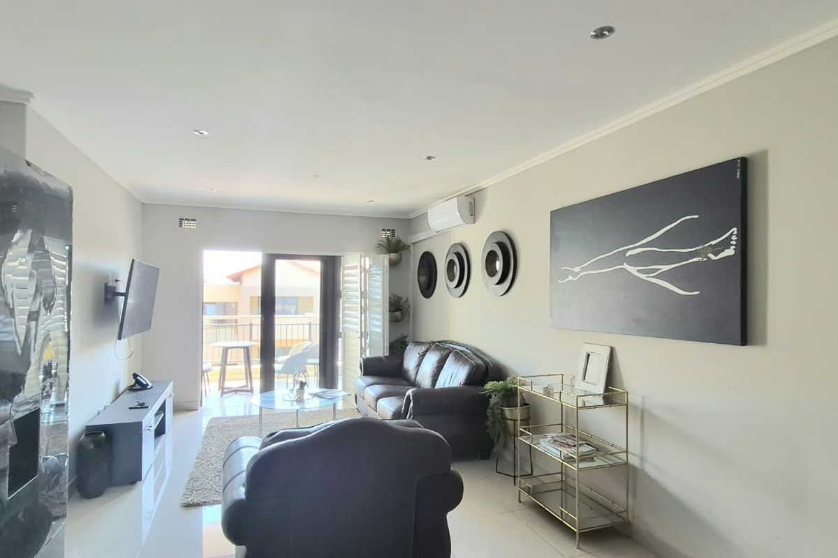 A well-maintained living room featuring tiled flooring, recessed downlighting, and a split-system air conditioner, with direct access to an outdoor balcony.
