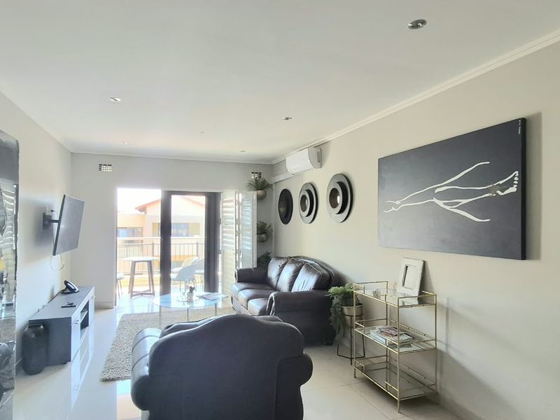 A well-maintained living room featuring tiled flooring, recessed downlighting, and a split-system air conditioner, with direct access to an outdoor balcony.