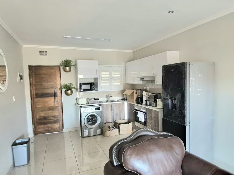 Open-plan kitchen area featuring modern white cabinetry, built-in oven, hob, extractor fan, and tiled flooring, seamlessly integrated into the living space.