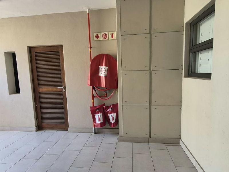 A clean, functional apartment hallway featuring tiled flooring, built-in storage cabinetry, and essential fire safety equipment including a hose reel and extinguishers.