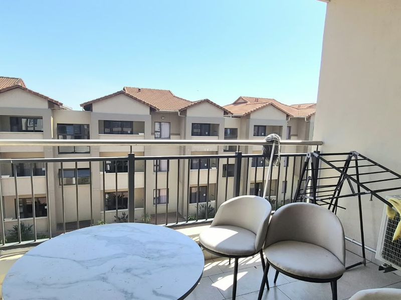 A private balcony featuring tiled flooring, a metal balustrade, and an external air conditioning unit, overlooking the apartment complex.