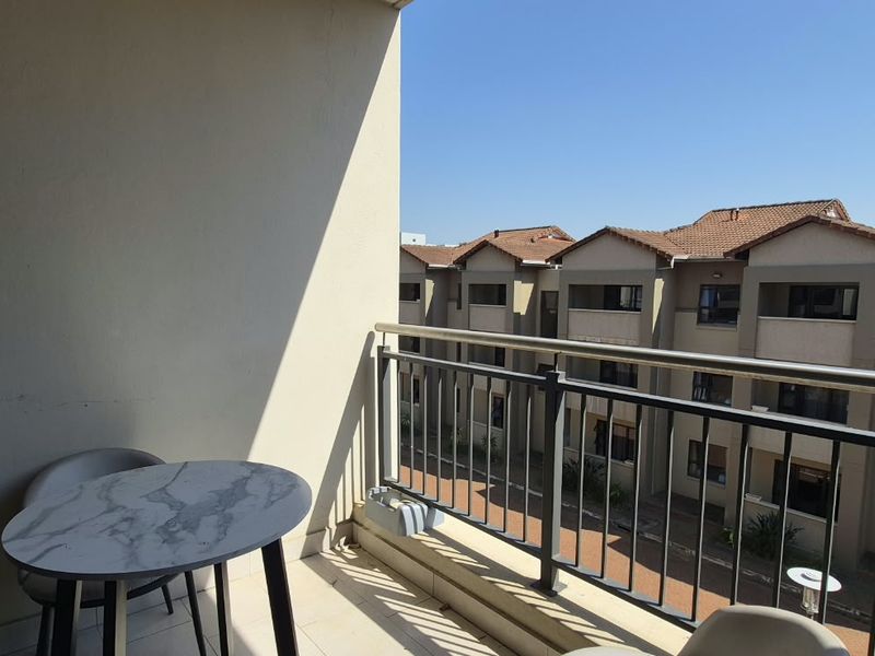 A private balcony featuring a metal balustrade and tiled flooring, offering an elevated view of the surrounding apartment complex.