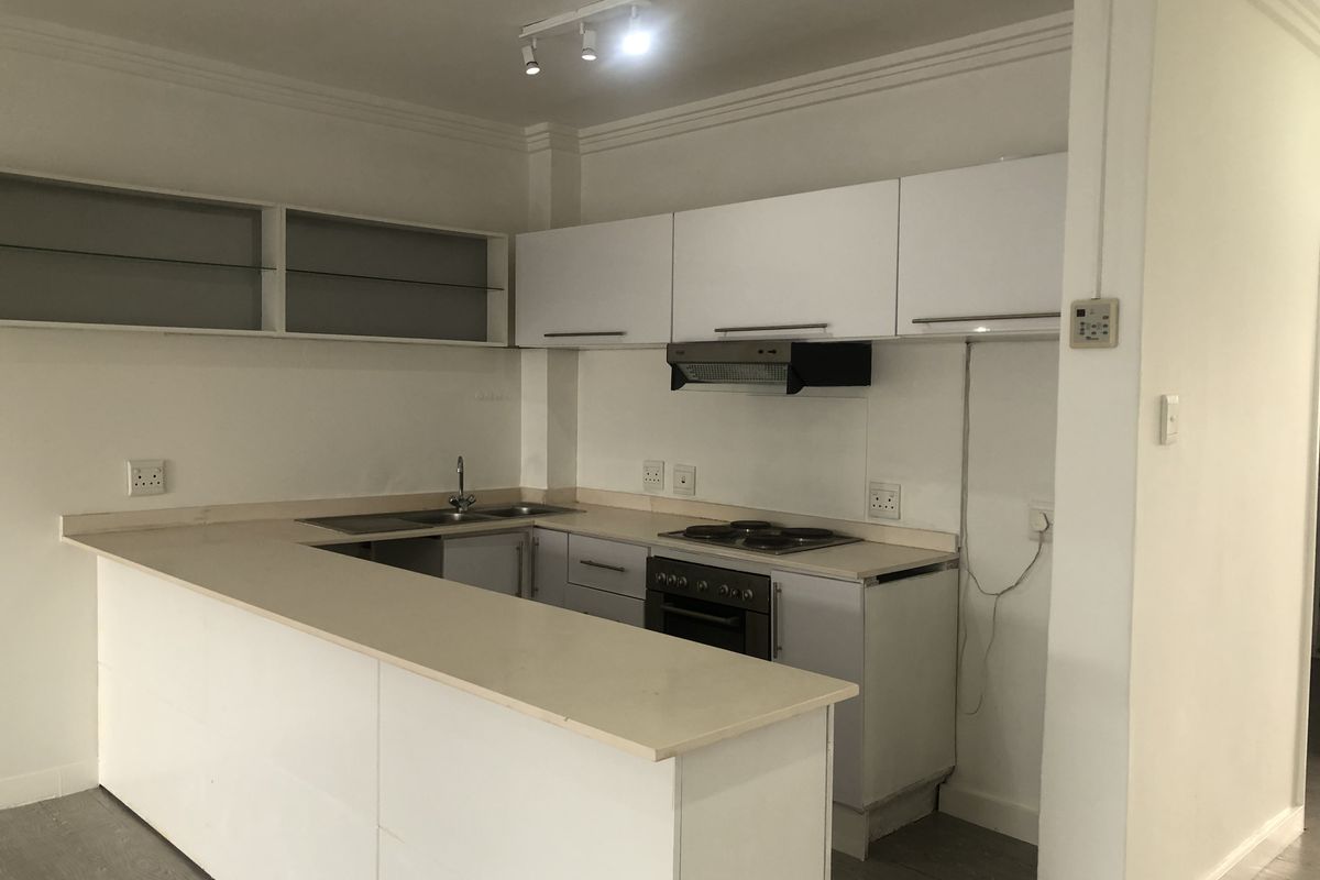 A functional kitchen featuring white cabinetry, a breakfast bar, integrated electric hob, oven, and extractor fan, with neutral finishes throughout.