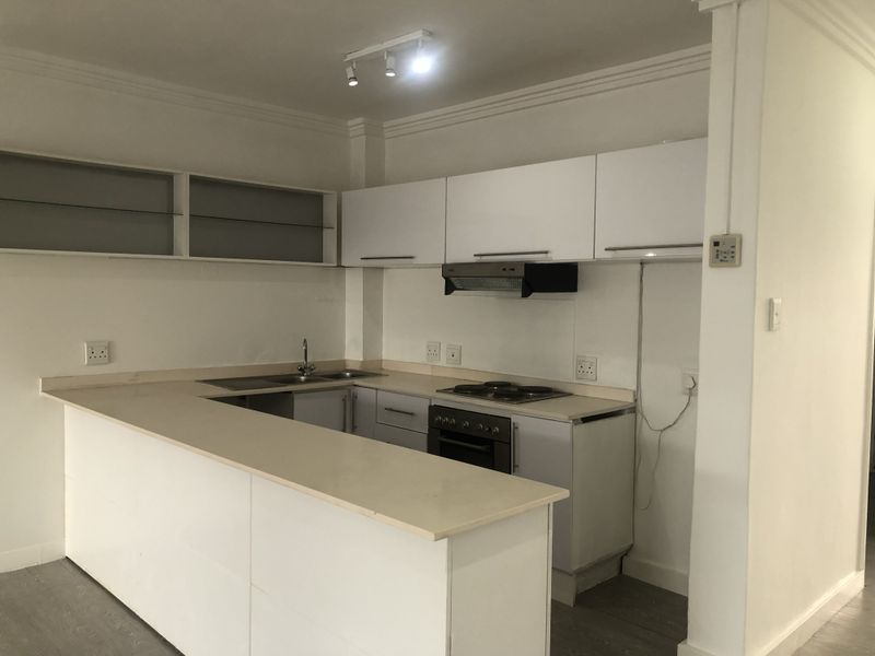 A functional kitchen featuring white cabinetry, a breakfast bar, integrated electric hob, oven, and extractor fan, with neutral finishes throughout.