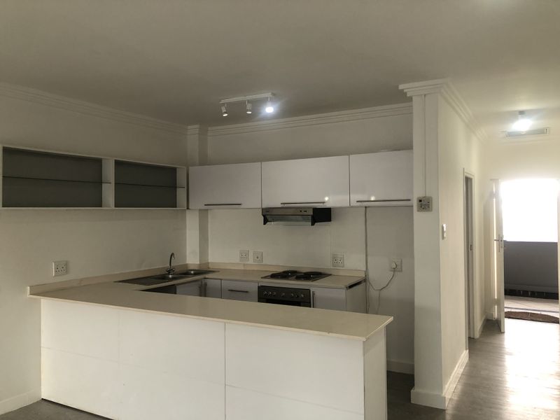 A functional kitchen featuring white cabinetry, a breakfast bar, built-in oven, and hob, with an open-plan layout leading to a hallway.