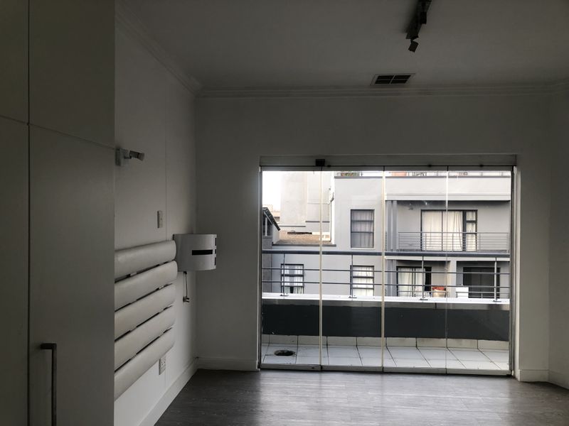 An empty bedroom featuring built-in cupboards, laminate flooring, and large sliding glass doors opening onto a private balcony.