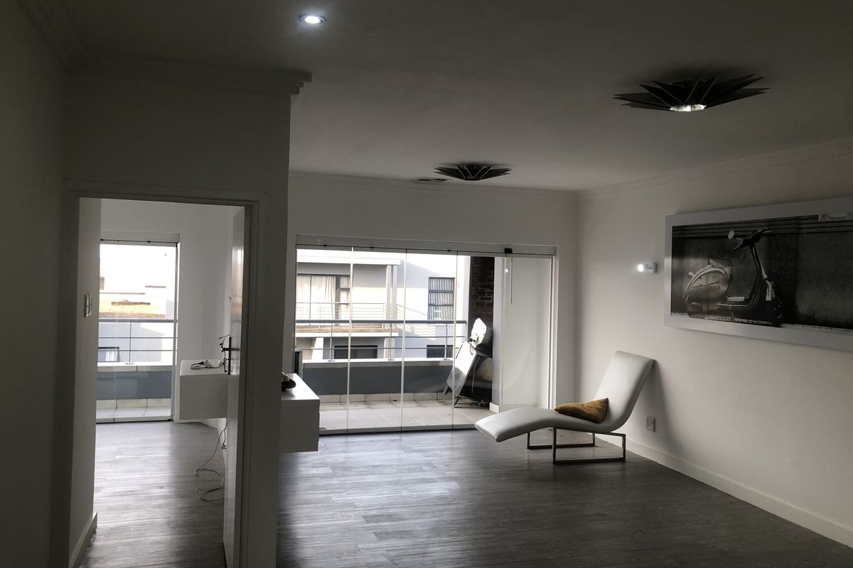Spacious living area featuring modern laminate flooring, recessed lighting, and large sliding glass doors providing access to an outdoor balcony.
