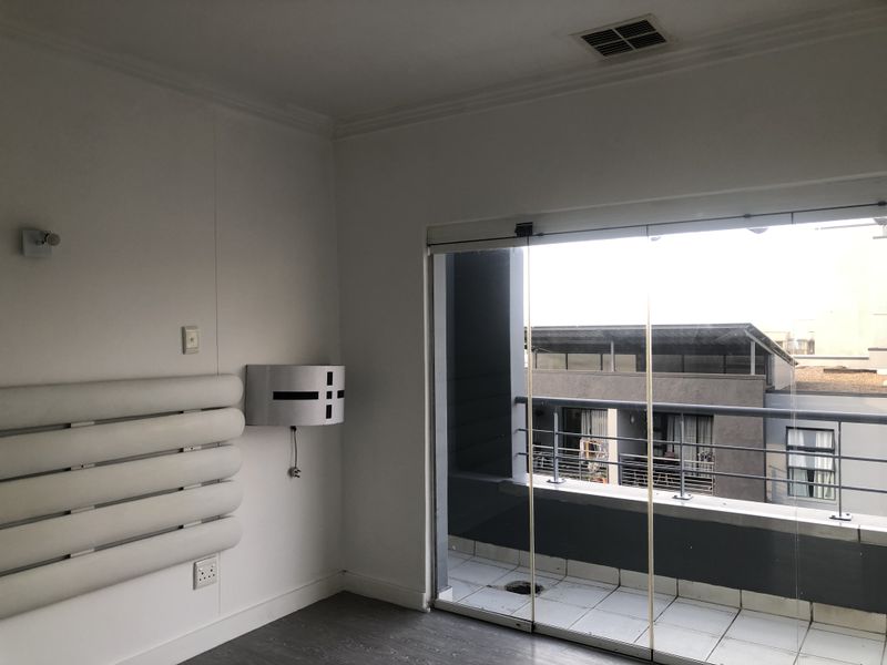 An empty bedroom featuring laminate flooring, a wall-mounted light fixture, and sliding glass doors leading to a private balcony.
