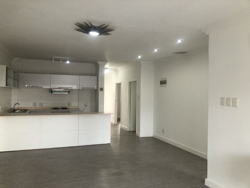 Spacious open-plan living area featuring a modern kitchen with built-in cabinetry, integrated hob, and extractor fan, finished with neutral tones and laminate flooring.