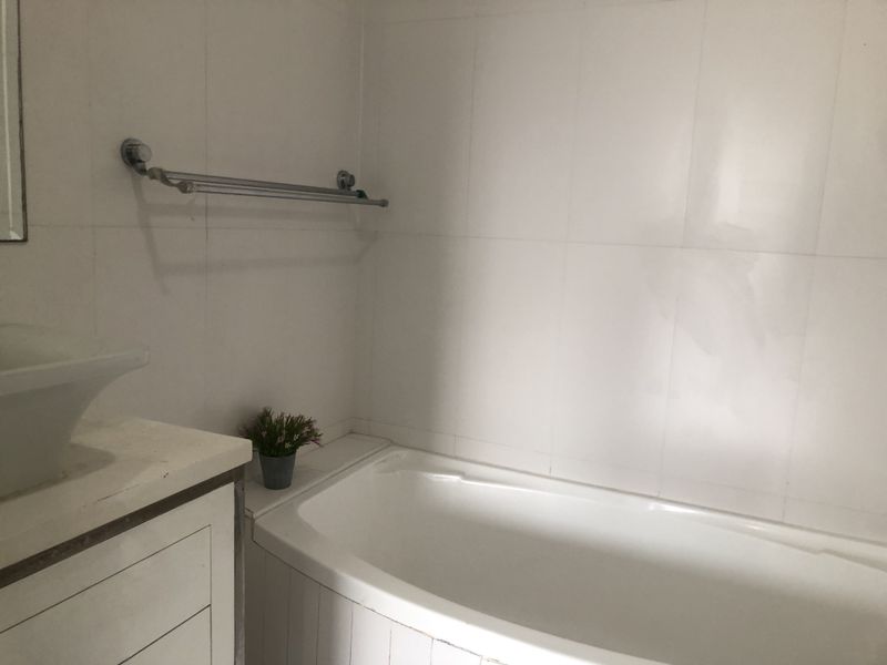 A compact bathroom featuring a built-in bathtub, a vessel sink vanity, and wall-mounted towel rail, requiring cosmetic updates to improve its overall condition.