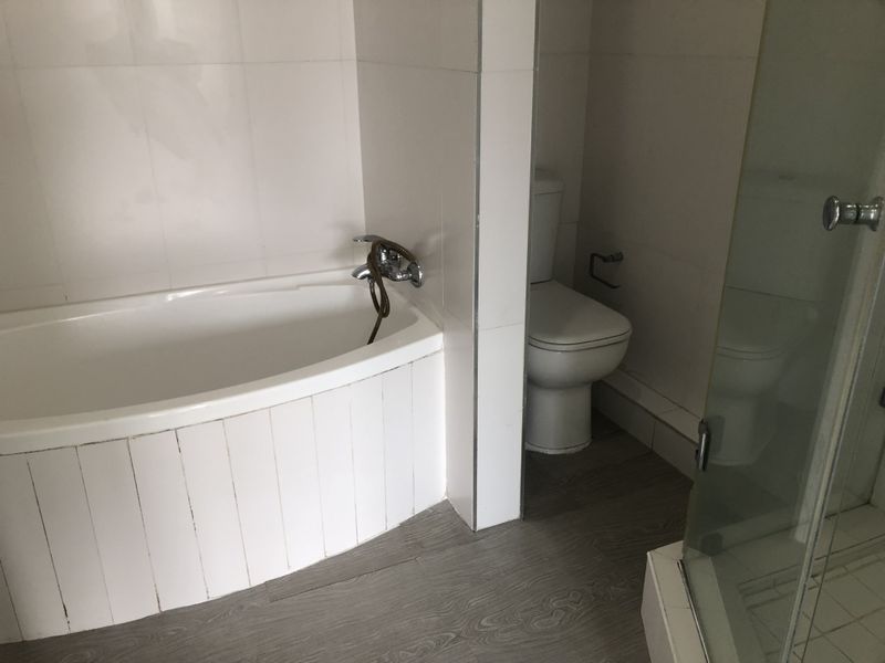 A functional bathroom featuring a bathtub, separate toilet area, and a glass-enclosed shower with neutral wall tiling and wood-look flooring.