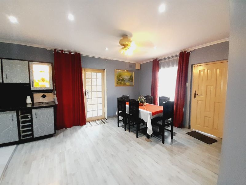 Open-plan living and dining area featuring light laminate flooring, recessed downlights, built-in cabinetry, and direct access to the exterior via a glass-panelled door.