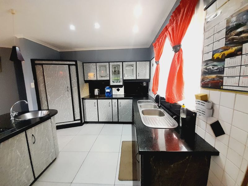 A functional kitchen featuring granite countertops, double stainless steel sinks, and ample built-in cabinetry with a modern marble-effect finish.
