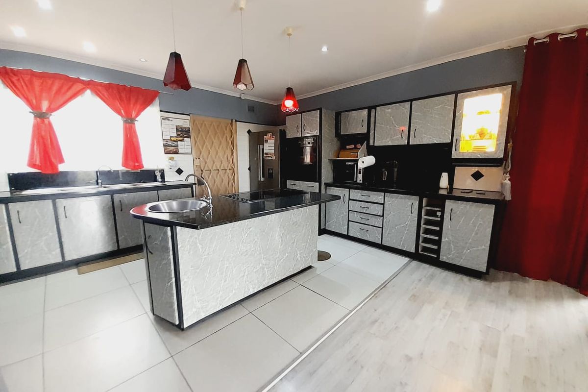 Modern kitchen featuring a central island with granite countertops, extensive built-in cabinetry, tiled flooring, and contemporary pendant lighting.