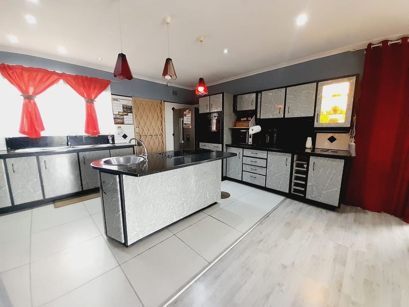 Modern kitchen featuring a central island with granite countertops, extensive built-in cabinetry, tiled flooring, and contemporary pendant lighting.