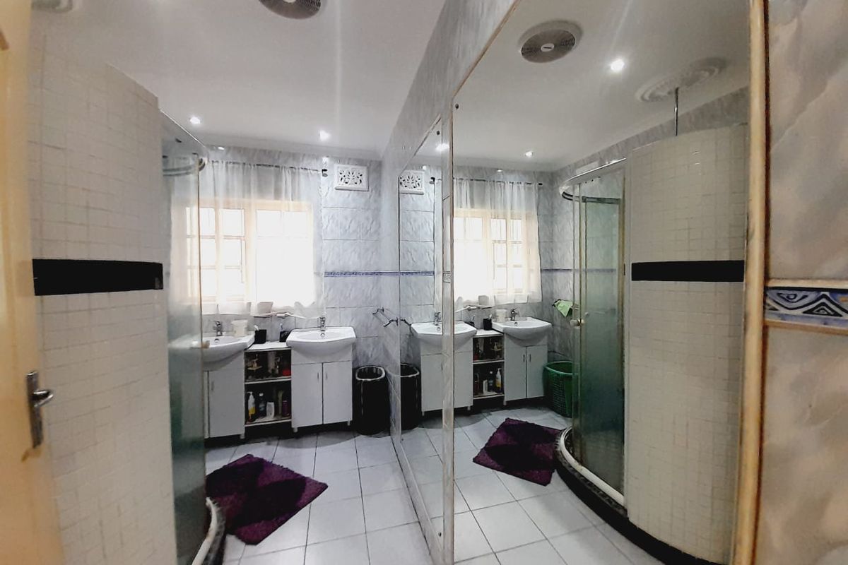 A functional bathroom featuring a dual vanity, a glass-enclosed shower, and floor-to-ceiling wall tiling with a large mirror.