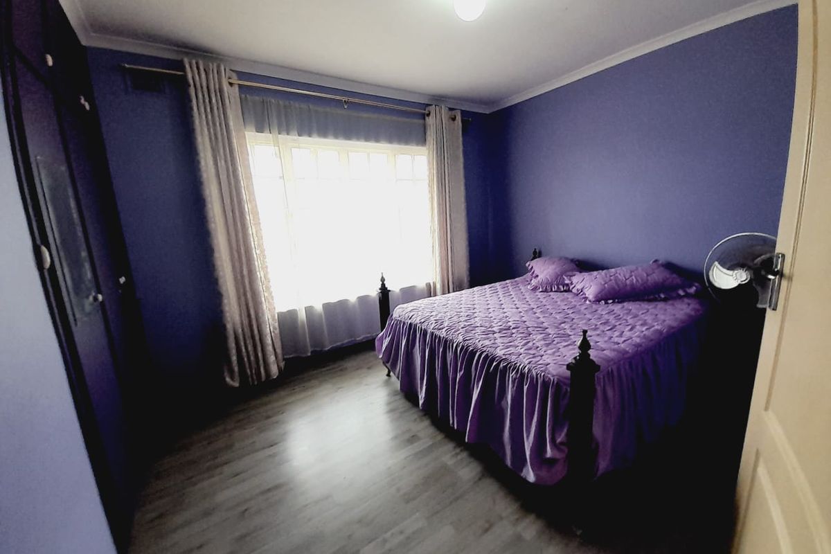 A bedroom featuring laminate flooring, built-in cupboards, and a large window allowing natural light.