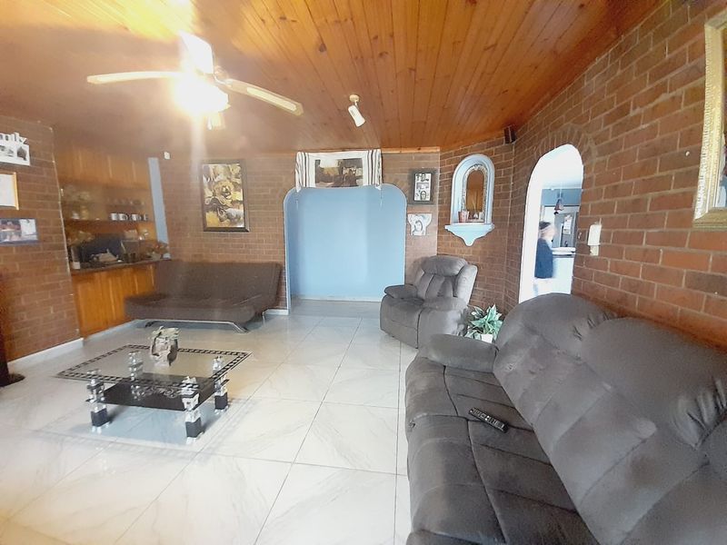 Spacious living room featuring exposed brick walls, timber ceiling, tiled flooring, and arched architectural details, offering a rustic aesthetic with potential for modernization.