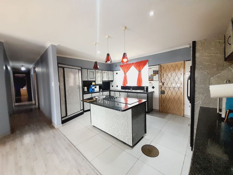 A functional kitchen featuring a central island with a built-in hob, stone countertops, ample cabinetry, and tiled flooring, leading into a hallway.