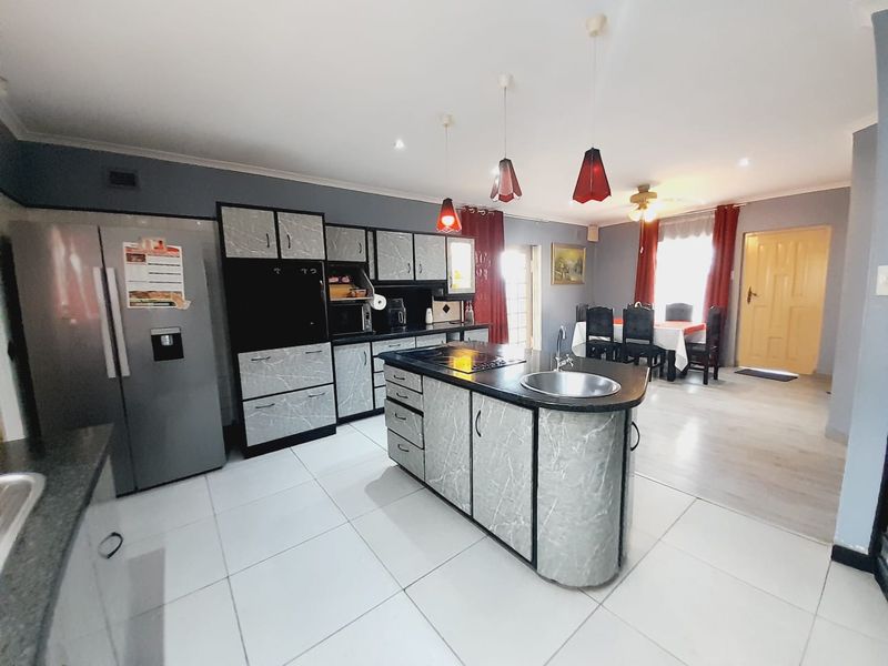 Open-plan kitchen and dining area featuring a central island with integrated sink, modern cabinetry, and tiled flooring throughout.